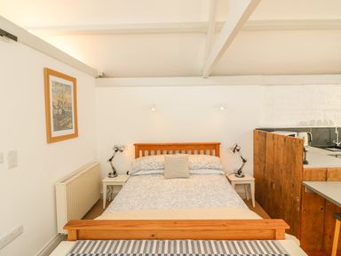 A bedroom with a wooden bed frame a patterned bedspread two bedside tables with lamps and a framed picture on the wall at The Daffodil Shed in Bere Alston