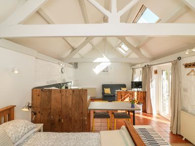 A studio room with a bed a dining table with yellow chairs a sofa and a wooden kitchen partition at The Daffodil Shed in Bere Alston