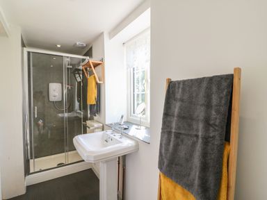 A bathroom with a glass shower enclosure a white pedestal sink towels on a rack and a window at The Daffodil Shed in Bere Alston