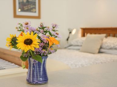 A vase with sunflowers and purple flowers on a table in a bedroom with a bed and pillow at The Daffodil Shed in Bere Alston