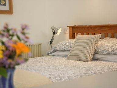 A bedroom with a wooden bed frame a striped pillow patterned bedding a metal desk lamp and flowers in a vase at The Daffodil Shed in Bere Alston