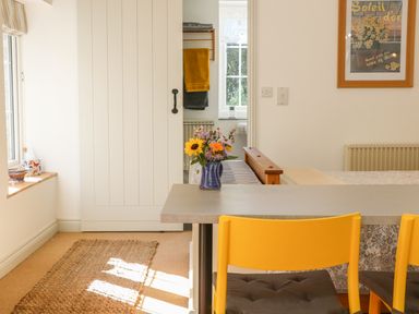 A dining area with yellow chairs a table with a vase of flowers a sliding door and a framed poster on the wall at The Daffodil Shed in Bere Alston