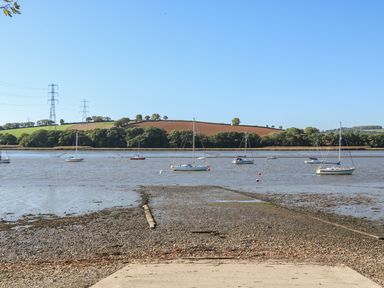 A boat ramp leading to a river with sailboats and grassy hills in the background at The Daffodil Shed in Bere Alston