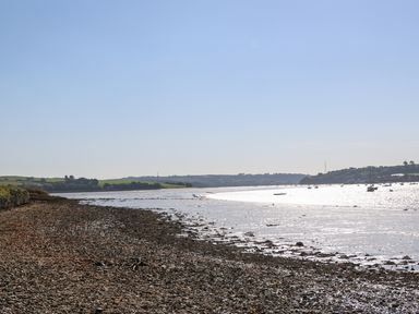 A rocky beach along a river with boats on the water and hills in the distance at The Daffodil Shed in Bere Alston