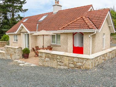 A house with a red tiled roof and a red door with a stone wall and outdoor table with chairs and umbrella at Cnoc suan in Aughavas County Leitrim