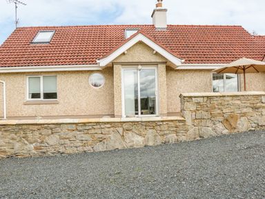 A house with a red tiled roof stone wall sliding glass door and patio umbrella at Cnoc suan in Aughavas County Leitrim
