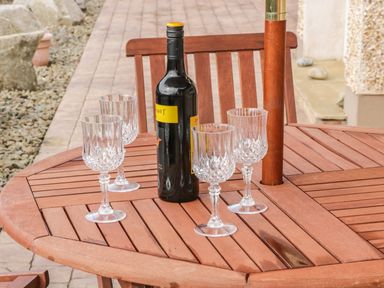A wooden outdoor table with four crystal wine glasses and a bottle of wine in a garden setting at Cnoc suan in Aughavas County Leitrim