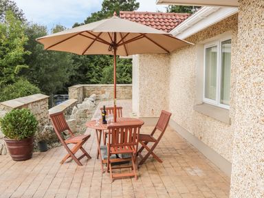 An outdoor patio area with a wooden table and chairs under a large beige umbrella surrounded by stone walls and greenery at Cnoc suan in Aughavas County Leitrim