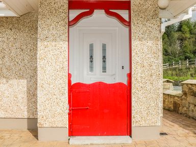 A red wooden gate in front of a white door with glass panels on a speckled exterior wall at Cnoc suan in Aughavas County Leitrim