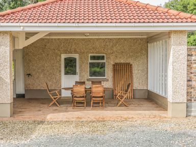 A covered patio area with wooden table and chairs and a white door at Cnoc suan Aughavas County Leitrim