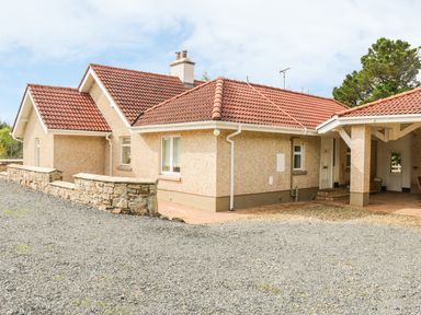 A single-story house with a red tiled roof and beige exterior walls with a stone wall and gravel driveway at Cnoc suan in Aughavas County Leitrim