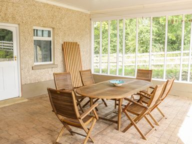 A covered patio with a wooden table and six wooden chairs and a window and door at Cnoc suan in Aughavas County Leitrim