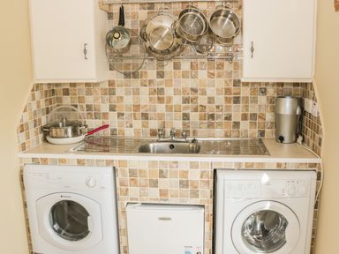 A kitchen area with a sink pots and pans hanging on the wall a washing machine and a dryer at Cnoc suan in Aughavas County Leitrim