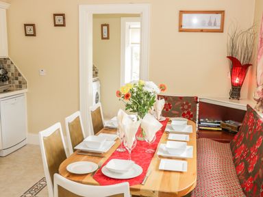 A dining area with a wooden table set with white plates and bowls flowers in a vase and chairs with a built in bench with cushions at Cnoc suan in Aughavas County Leitrim