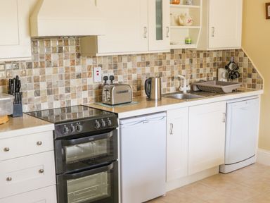 A kitchen with white cabinets a black oven a toaster a kettle a sink and a dishwasher at Cnoc suan in Aughavas County Leitrim