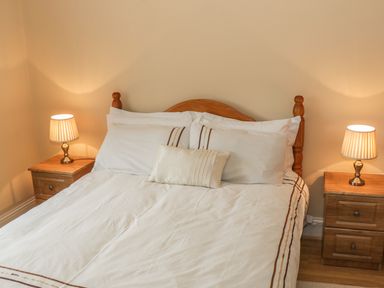 A bedroom with a wooden bed frame two bedside tables with lamps and white bedding at Cnoc suan in Aughavas County Leitrim