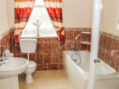 A bathroom with a sink toilet and bathtub with red curtains on a window at Cnoc suan in Aughavas County Leitrim