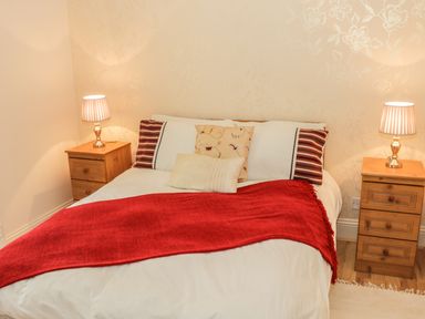 A bedroom with a double bed with cushions and a red throw with wooden bedside tables and lamps at Cnoc suan in Aughavas County Leitrim