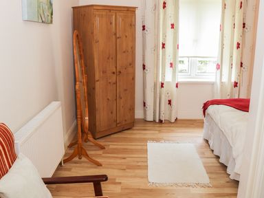 A bedroom with a wooden wardrobe a standing mirror a bed with a white bedspread and red throw and a white rug on the wooden floor at Cnoc suan in Aughavas County Leitrim