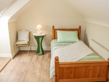 A wooden single bed with green bedding beside a green bedside table with a lamp and a chair in a room at Cnoc suan in Aughavas County Leitrim