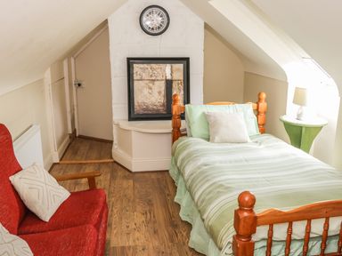 A bedroom with a single wooden bed with green striped bedding and a red armchair with pillows at Cnoc suan in Aughavas County Leitrim