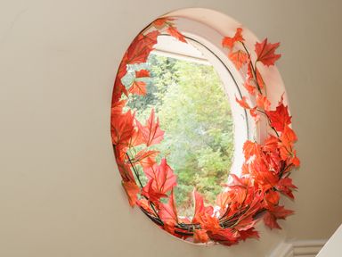 A circular window decorated with artificial red leaves with green trees visible outside at Cnoc suan in Aughavas County Leitrim