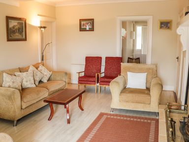 A living room with a beige sofa and armchair red chairs and a wooden coffee table at Cnoc suan in Aughavas County Leitrim