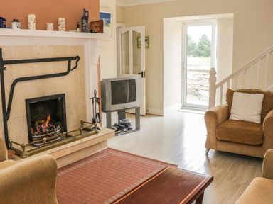 A living room with a fireplace a television armchairs and a wooden table at Cnoc suan in Aughavas County Leitrim
