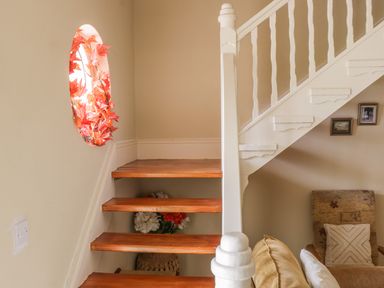 A staircase with wooden steps and white railing next to a wall with a circular window decorated with orange leaves and a seating area with a beige cushion at Cnoc suan in Aughavas County Leitrim
