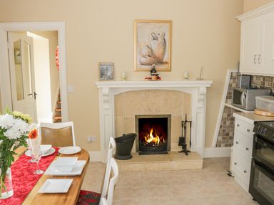 A kitchen dining area with a fireplace a dining table set with plates and flowers and kitchen appliances at Cnoc suan in Aughavas County Leitrim