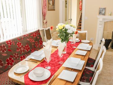 A dining room with a wooden table set with white plates bowls and glasses and a floral centerpiece at Cnoc suan in Aughavas County Leitrim