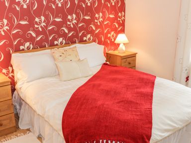 A bedroom with a bed with white bedding and red throw a bedside table with a lamp and a red floral wallpaper at Cnoc suan in Aughavas County Leitrim
