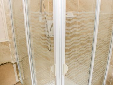 A shower cubicle with glass doors and a handheld showerhead in a tiled bathroom at Cnoc suan in Aughavas County Leitrim