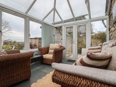 A conservatory with rattan chairs and glass doors at The Smithy in Blisland