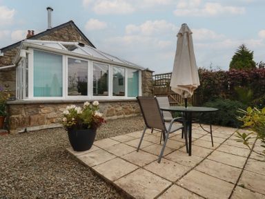 A garden with a table, chair, and umbrella near a conservatory at The Smithy in Blisland
