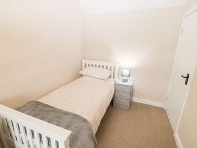 A small bedroom with a single bed a bedside table with lamp and a closed door at 3 Green Terrace in Llangaffo near Newborough