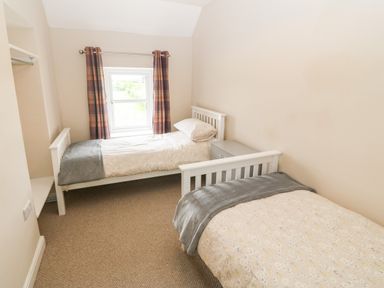 A bedroom with two single beds a window with curtains and a bedside table at 3 Green Terrace in Llangaffo near Newborough