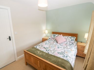 A bedroom with a wooden bed with floral bedding and two bedside tables with lamps at 3 Green Terrace in Llangaffo near Newborough