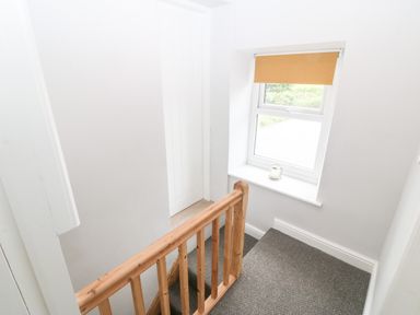 A stair landing with a wooden banister a window with a roller blind and a candle on the windowsill at 3 Green Terrace in Llangaffo near Newborough