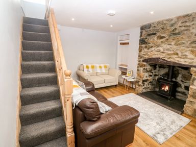 A living room with a stone fireplace a wood-burning stove two sofas a rug and carpeted stairs at 3 Green Terrace in Llangaffo near Newborough