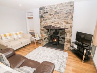 A living room with a stone fireplace a wood burning stove two sofas a TV on a stand and two side tables at 3 Green Terrace in Llangaffo near Newborough