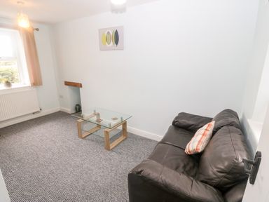 A small living room with a black leather sofa and glass coffee table at 3 Green Terrace in Llangaffo near Newborough
