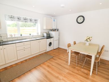 A kitchen with white cabinets, a washing machine, refrigerator, microwave, dining table with four chairs and a clock on the wall at 3 Green Terrace in Llangaffo near Newborough