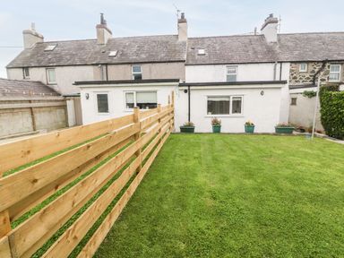 A backyard with a wooden fence and grass in front of a row of terraced houses at 3 Green Terrace in Llangaffo near Newborough