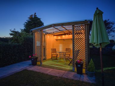 An outdoor patio area with wooden chairs and a round table under a pergola at 3 Green Terrace in Llangaffo near Newborough