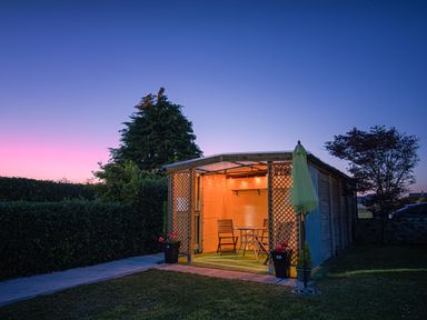 An outdoor wooden gazebo with table and chairs lit up at dusk at 3 Green Terrace in Llangaffo near Newborough