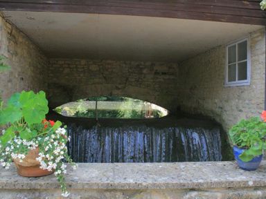 A stone structure with a small waterfall and two flower pots on a ledge at Lime Tree in Burford