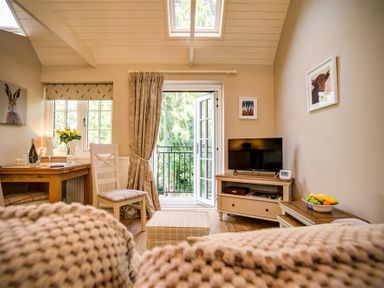 A living room with a table and chairs a tv on a stand and an open door leading outside at Lime Tree in Burford