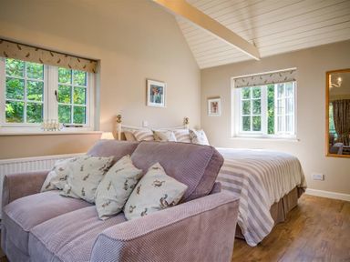 A bedroom with a bed and a sofa with cushions near two windows at Lime Tree in Burford