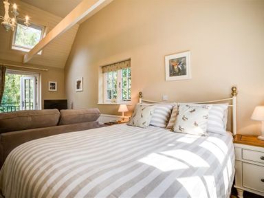 A bedroom with a bed a sofa nightstands lamps and a window at Lime Tree in Burford